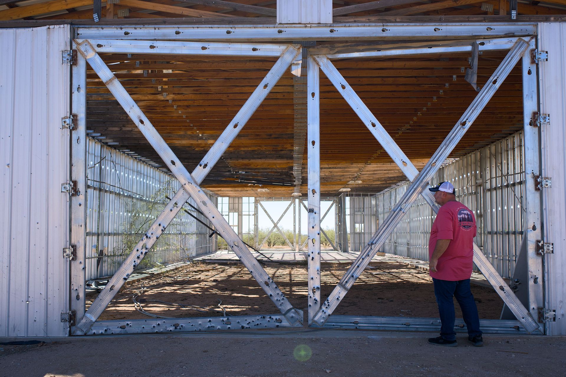 A man in a pink shirt examines a large metal framework under construction. Sunny weather.