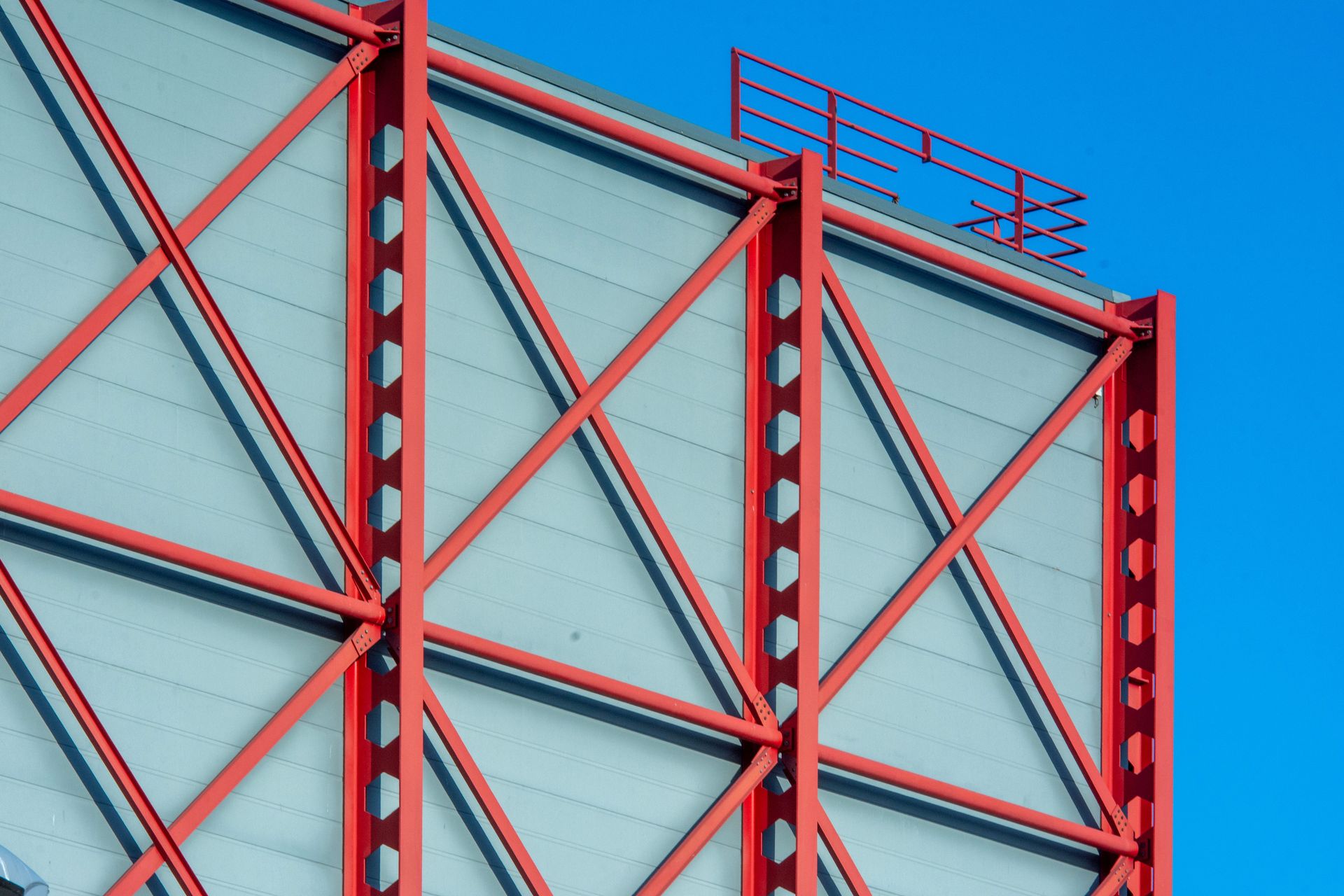 Close-up of a modern building facade featuring red steel beams in geometric patterns against a blue sky.